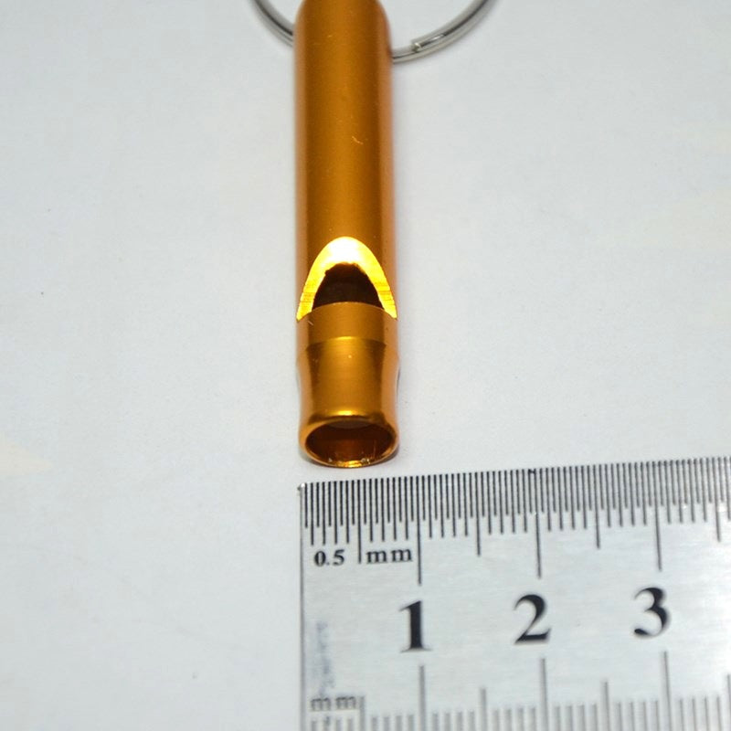 Gold rescue whistle keychain with a ruler for scale on a white background