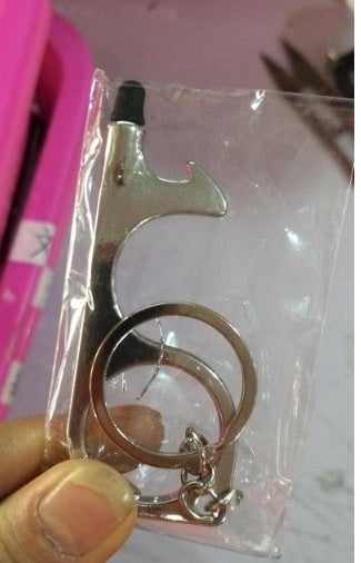 A door opener keychain with a key ring, packaged in a clear plastic bag and held by a hand.