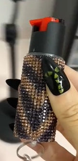 Decorative pepper spray with rhinestones held by a hand with black nail polish.