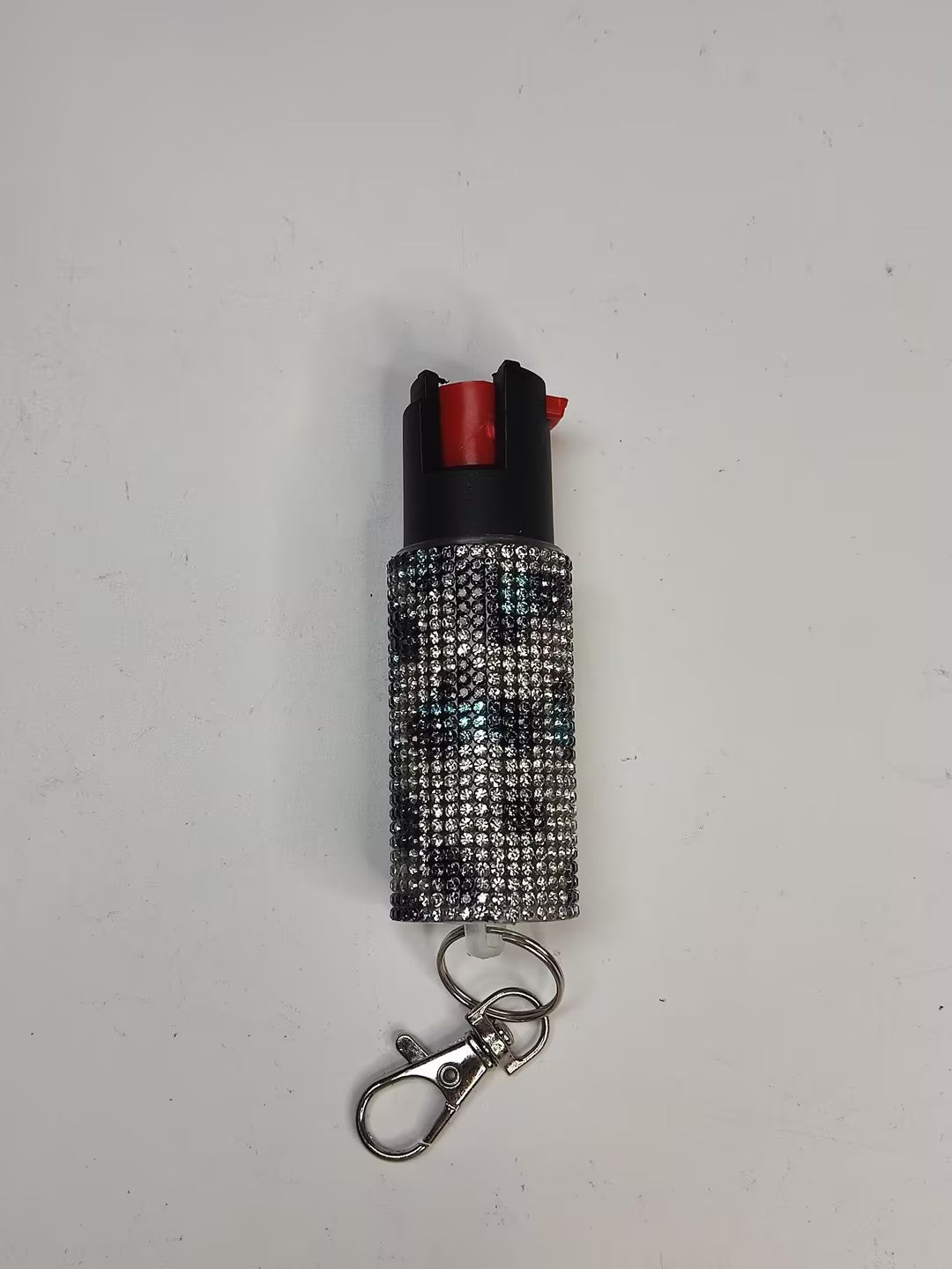 Small pepper spray device with rhinestone case and keychain on a light gray background